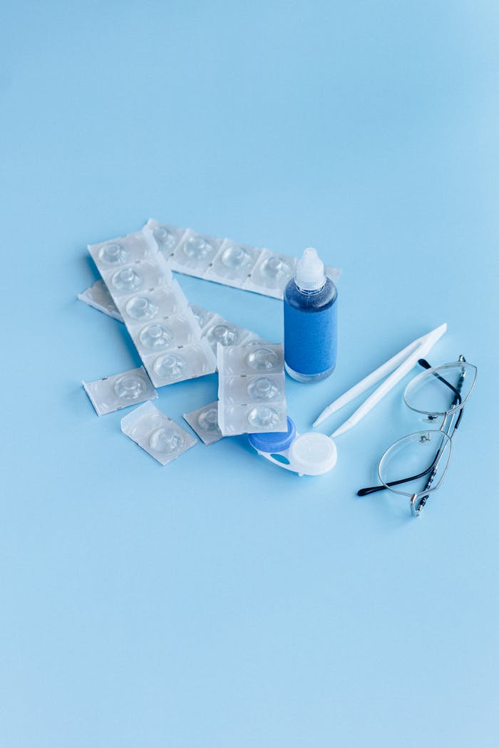 Close-up of contact lens care items including solution, case, and glasses on a blue backdrop.
